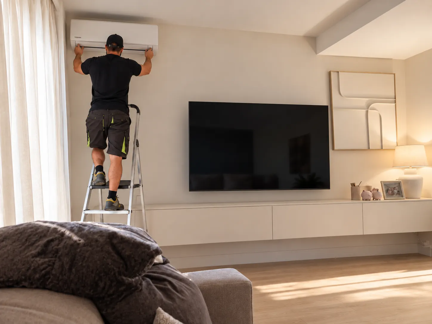 Technician on a stepladder fitting a white wall-mounted air conditioner in a bright Costa del Sol living room
